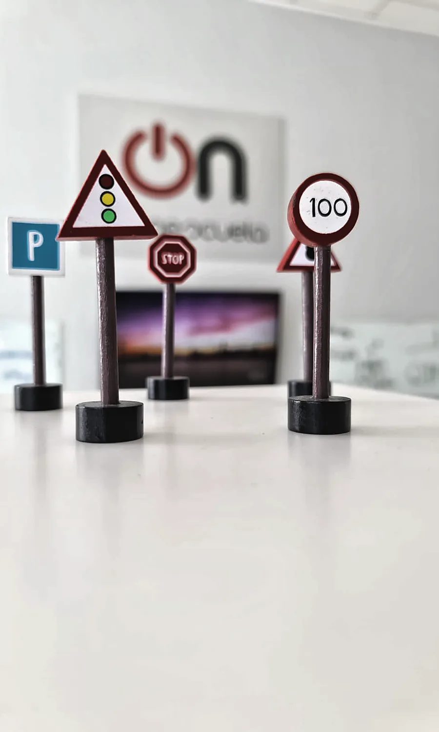 Señales de tráfico en miniatura sobre una mesa del aula, con el logotipo de autoescuela ON al fondo